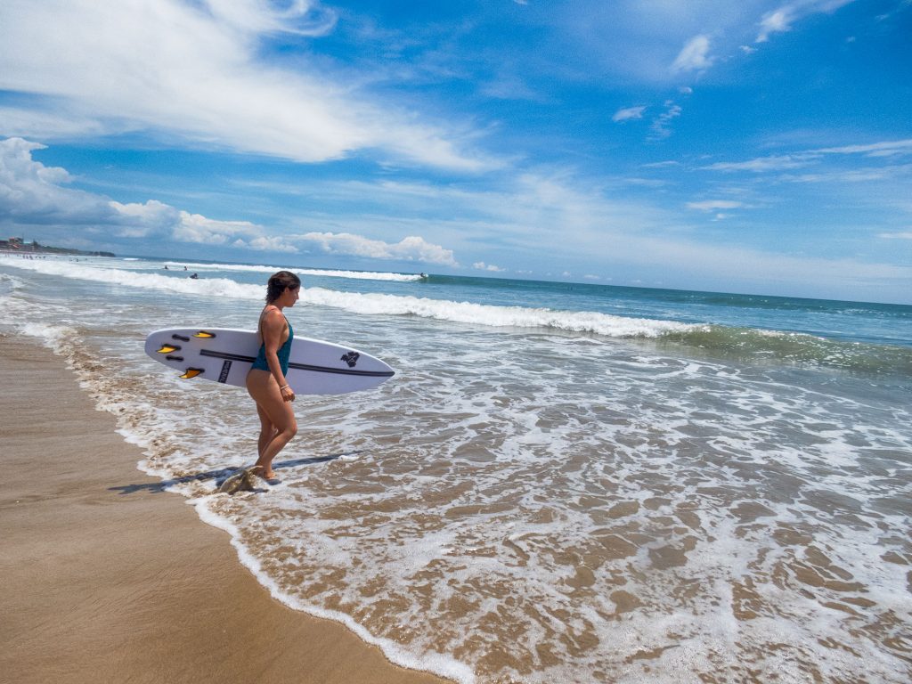 woman entering ocean with surfboard