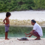 boy and grandfather cutting a fish on the beach